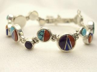 Genuine Turquoise, Spiny Oyster Shell, Sugilite, Mother of Pearl and Blue Lapis inlaid between ribbons of Sterling Silver. Beautiful channel inlay design. Designed by Navajo Artist Calvin Begay. Signed. 
