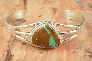 Genuine Boulder Turquoise set in Sterling Silver Bracelet. The cabochon is Boulder Turquoise, you can see the veins of Turquoise running through the host rock. The Boulder Turquoise Mine is located in northeast Nevada. It was discovered in 1970 by a Shoshone sheep herder. Production is small due to the remote location and winter weather. Boulder Turquoise is valued for both it's beauty and rarity. Every stone is unique. Created by Navajo Artist Larson Lee. Signed by the artist.