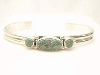 Genuine Number 8 Turquoise set in Sterling Silver. Stunning heavy gauge Sterling Silver Bracelet with 3 Beautiful Turquoise Stones. The Number 8 mine is located in Eureka County Nevada. Since 1976 there has been no Number 8 Turquoise mined. There is however, an existing stock pile that Mr. Dowell Ward, the last owner of the Number 8 mine, had stocked away for later sorting. The Turquoise is a collector's item--because once the reserve is gone there will be no more material released onto the market. The Gold Mining Company owns the claim to the Number 8 mine and it has been swallowed up by the gold mining operations. This is some of the last Number 8 Turquoise to be had and will be a great addition to your collection. Created by Navajo Artist Milton Lee. Signed.
