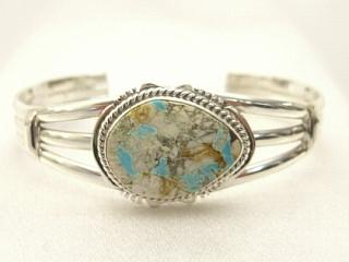 Genuine Boulder Turquoise set in Sterling Silver Bracelet. The cabochon is Boulder Turquoise, you can see the veins of Turquoise running through the host rock. The Boulder Turquoise Mine is located in northeast Nevada. It was discovered in 1970 by a Shoshone sheep herder. Production is small due to the remote location and winter weather. Boulder Turquoise is valued for both it's beauty and rarity. Every stone is unique. Created by Navajo Artist John Nelson. Signed.