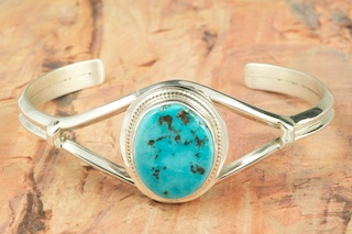 Genuine Boulder Turquoise set in Sterling Silver Bracelet. The cabochon is Boulder Turquoise, you can see the veins of Turquoise running through the host rock. The Boulder Turquoise Mine is located in northeast Nevada. It was discovered in 1970 by a Shoshone sheep herder. Production is small due to the remote location and winter weather. Boulder Turquoise is valued for both it's beauty and rarity. Every stone is unique. Created by Navajo Artist Larson Lee. Signed.
